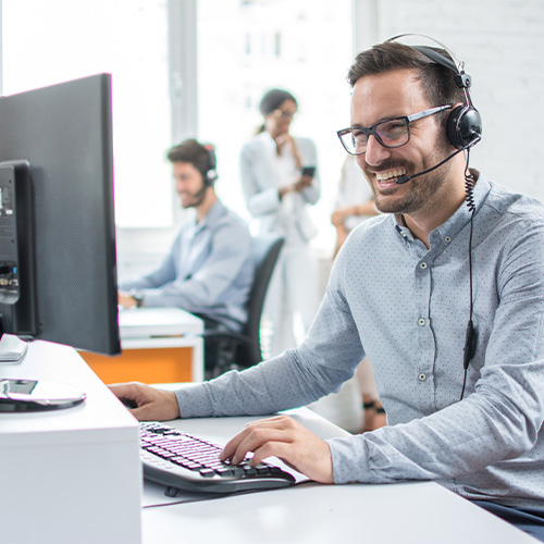 Smiling customer support operator with hands-free headset working in the office.